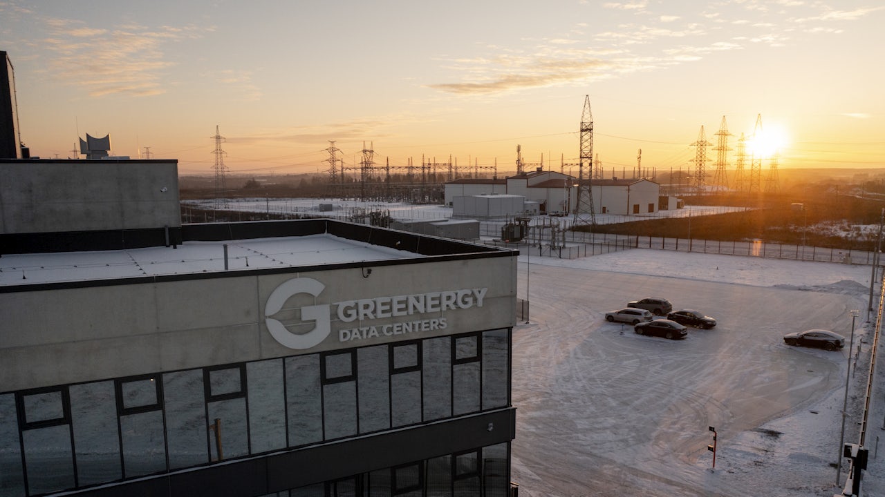 A person is standing in a field with a large rock in the background.