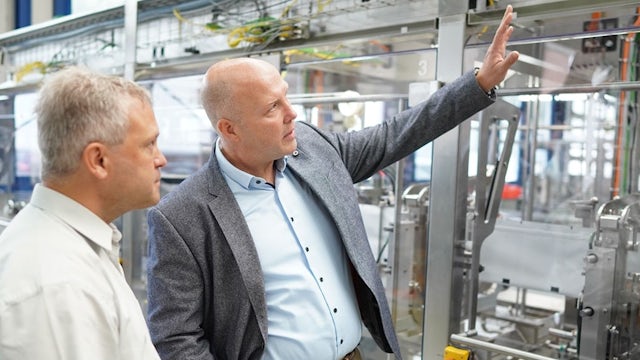 Two men in a manufacturing plant, looking at a machine and having a conversation.