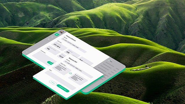 Hand holding small green plant sprouting from soil against backdrop of wind turbines