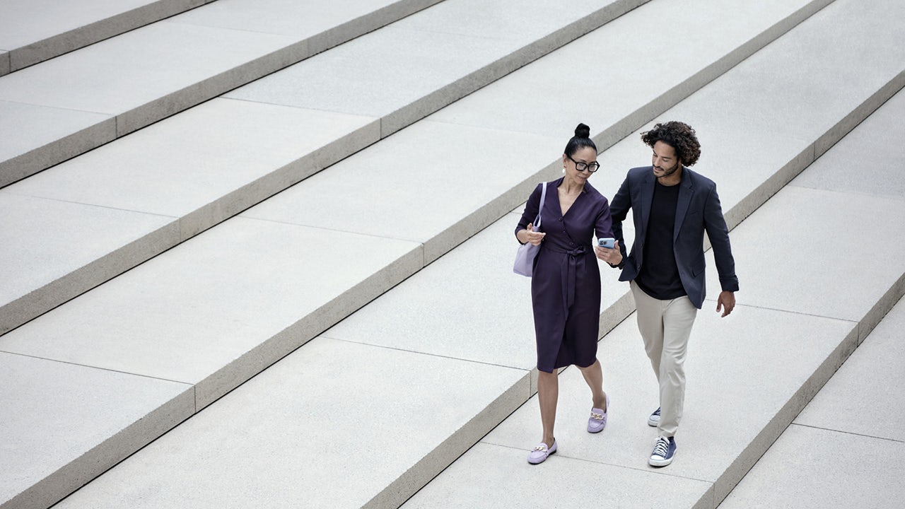 Young man and woman walking across cement steps looking at a mobile device together.