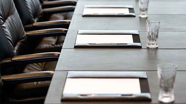 A boardroom table is set with notepads and drinking glasses.