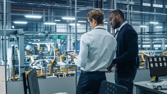 Two engineers discussing operational analytics on a tablet next to am automated assembly line