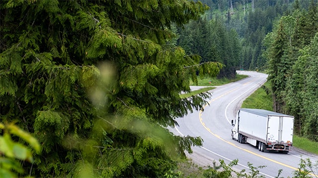 Semi-truck traveling down a winding road through forests.