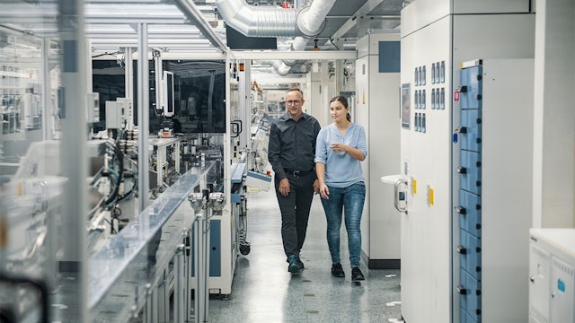 Two workers walking through industry floor assessing control panels.