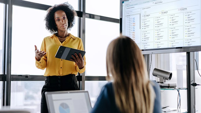 Coworkers interacting in front of large screen.
