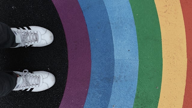 Shoes in front of a rainbow painted on asphalt.