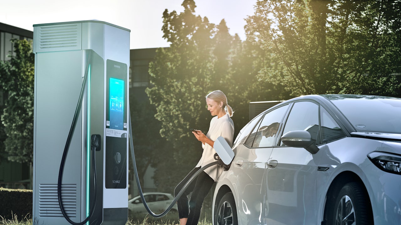 Woman standing at an electric charger, charging her vehicle.
