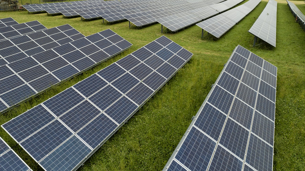 A solar panel installation in the Azores, Portugal, with a clear blue sky and a mountain range in the background.