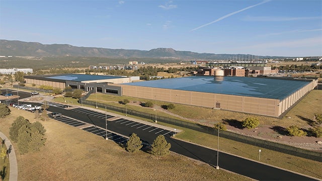 Aerial view of sprawling data center with parking lot in foreground and mountains in the background.  