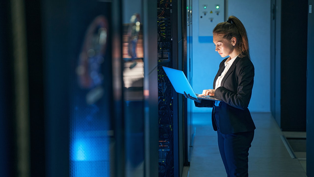 Woman standing with laptop in front of data center.