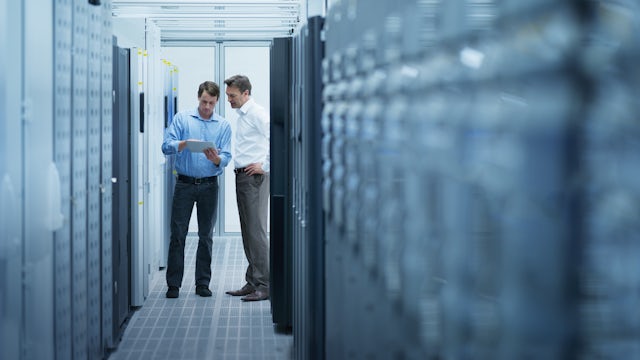 two men standing in a data center looking at data on a tablet.