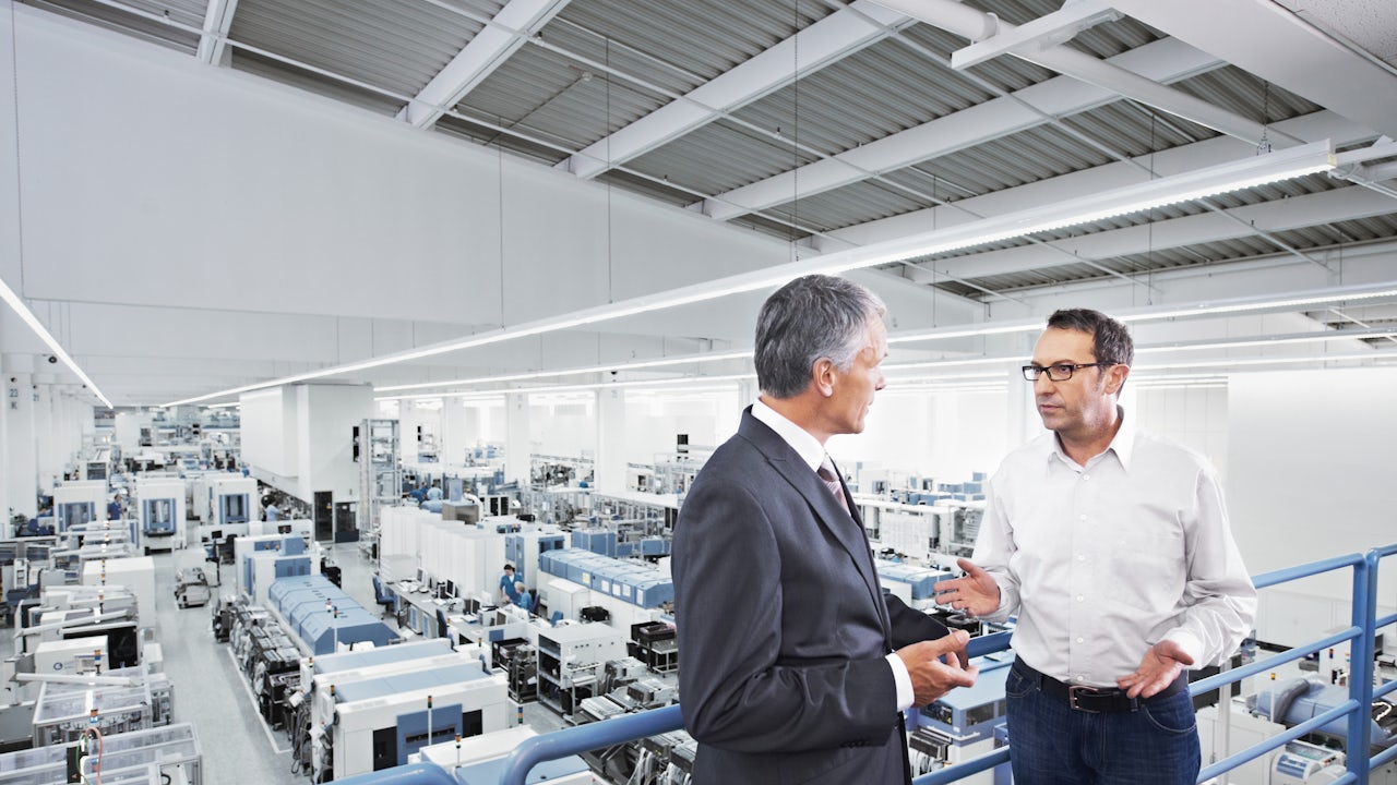 Person in black clothing standing against white wall with black border, holding a dark object.