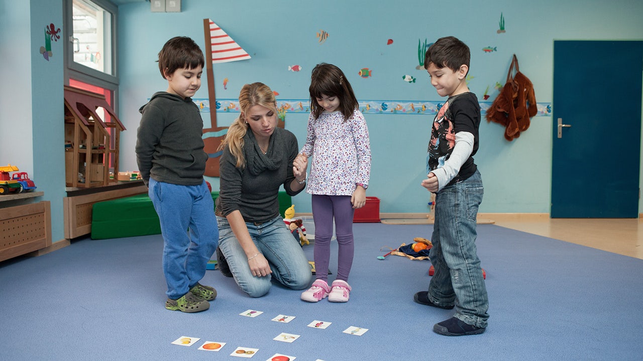A group of young children in a classroom setting, engaged in learning activities with their teacher.
