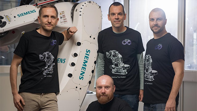 Three men in black t-shirts with a "3D" logo and "Machine Tool Robot" graphic stand beside a large white Siemens industrial robot.