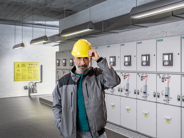 Man in hardhat standing in front of medium-voltage switchgear, representing electrification and automation.
