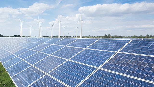 The image shows a field with wind turbines and solar panels.