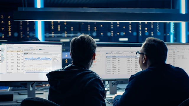 Two people gaze into glowing monitors in an office setting.
