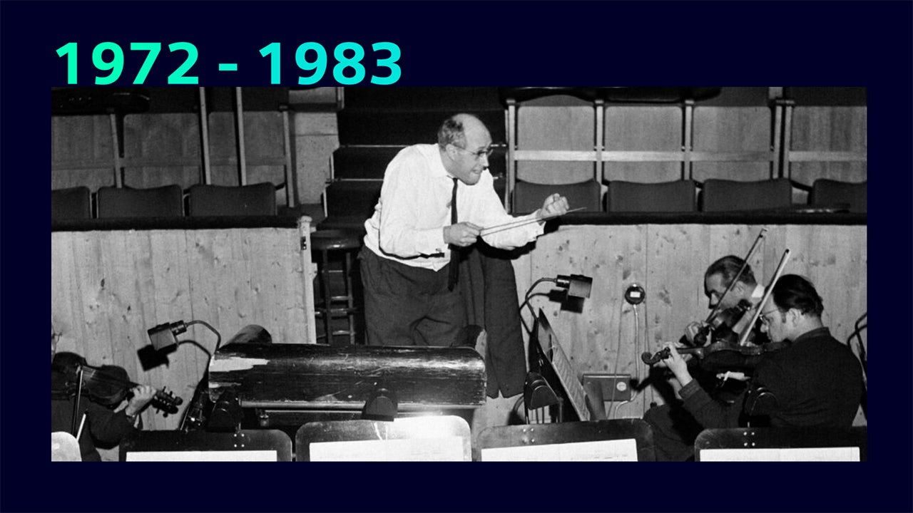 A person in a suit and tie standing in front of a building with a large window.