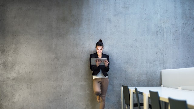 A woman leaning against the wall holding a tablet.