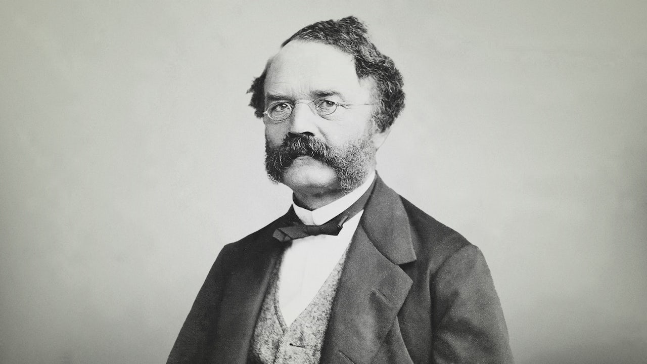 A black and white photograph of a man in a suit and tie, possibly from the late 1800s or early 1900s.