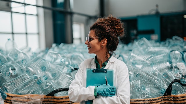 A female worker in a factory is filling bottles with liquid, likely in a beverage production facility.
