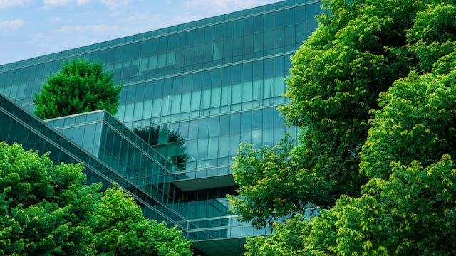 Glass building with green trees in front against a blue sky.
