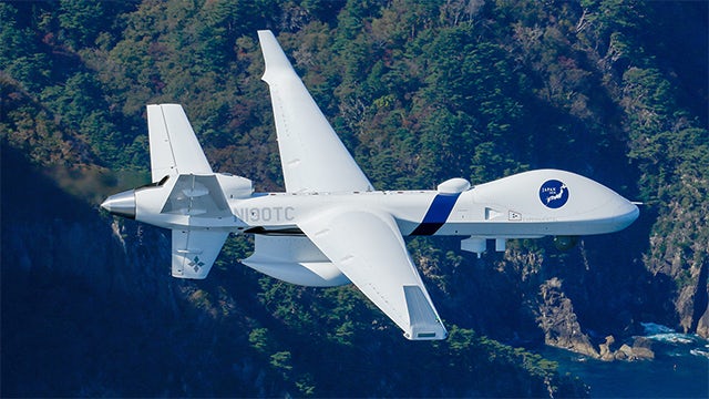 A person in a suit and tie stands in front of a large screen displaying a graph and text.