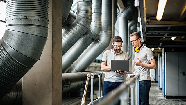 A person in a blue shirt and mask stands in front of a blue wall with a white sign, holding a blue object.