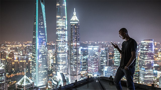 Man holding phone with a nighttime city skyline in the background.