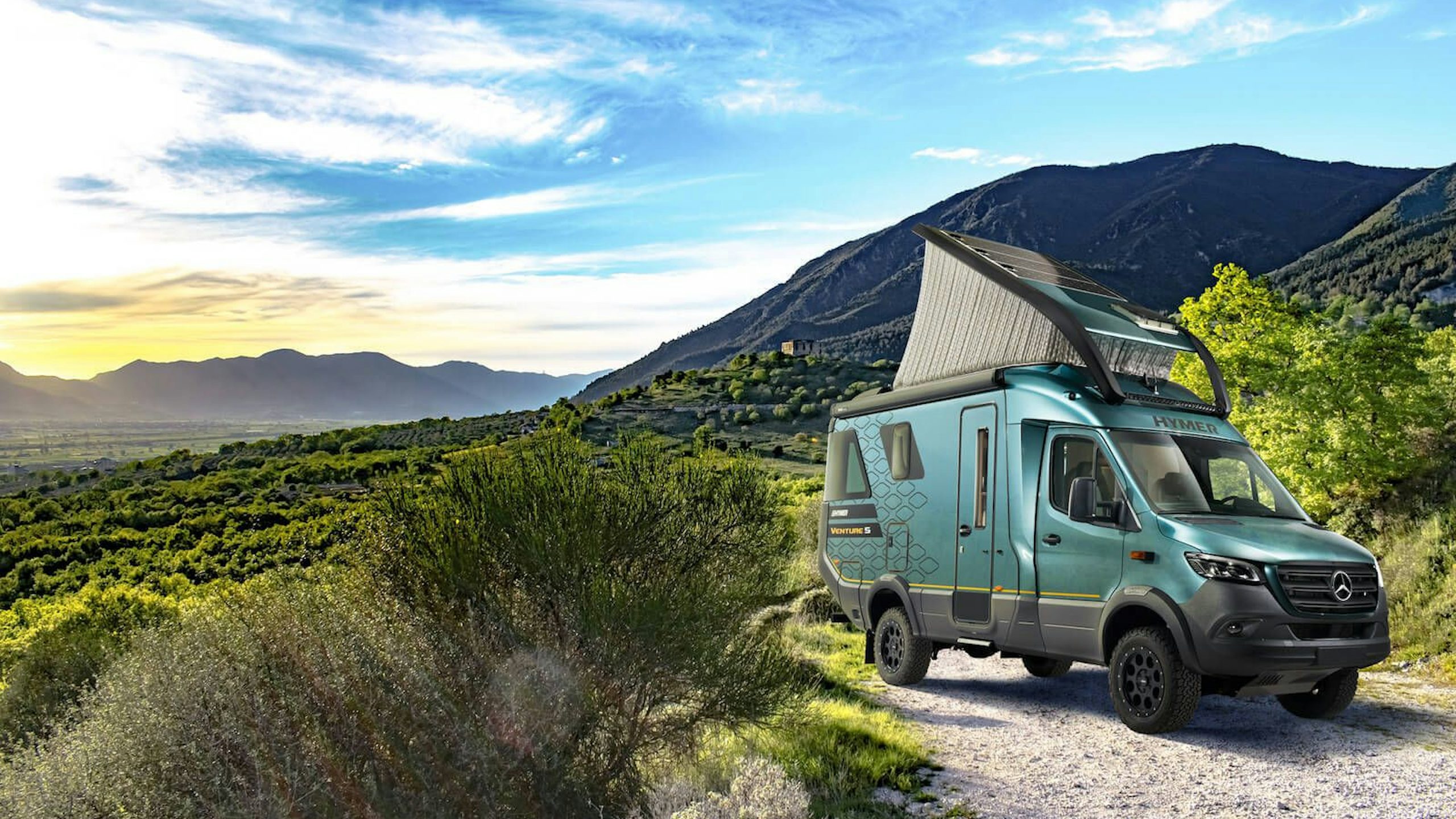A landscape image of a Hymer Vemture S van parked in a scenic outdoor area with mountains in the background. 