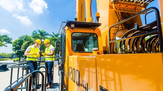 Two men in hard hats working next to a large piece of machinery.