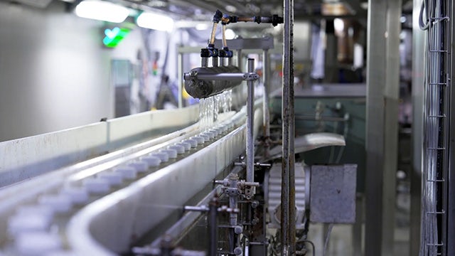 Close-up view of an industrial production line with metal piping, nozzles, and conveyor equipment inside a manufacturing facility.