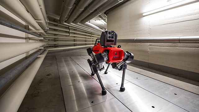 An AI-enabled robot dog with a red body and metal arms is moving along an industrial duct looking for inconsistencies.