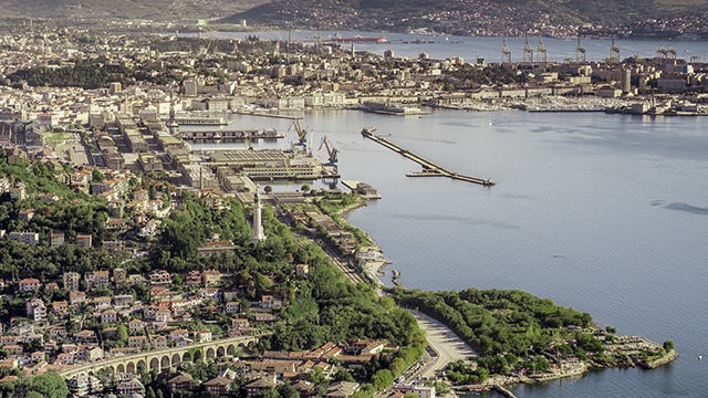 Aerial view of Trieste, Italy, with its coastline and port area, illustrating the energy grid partnership with Siemens.  