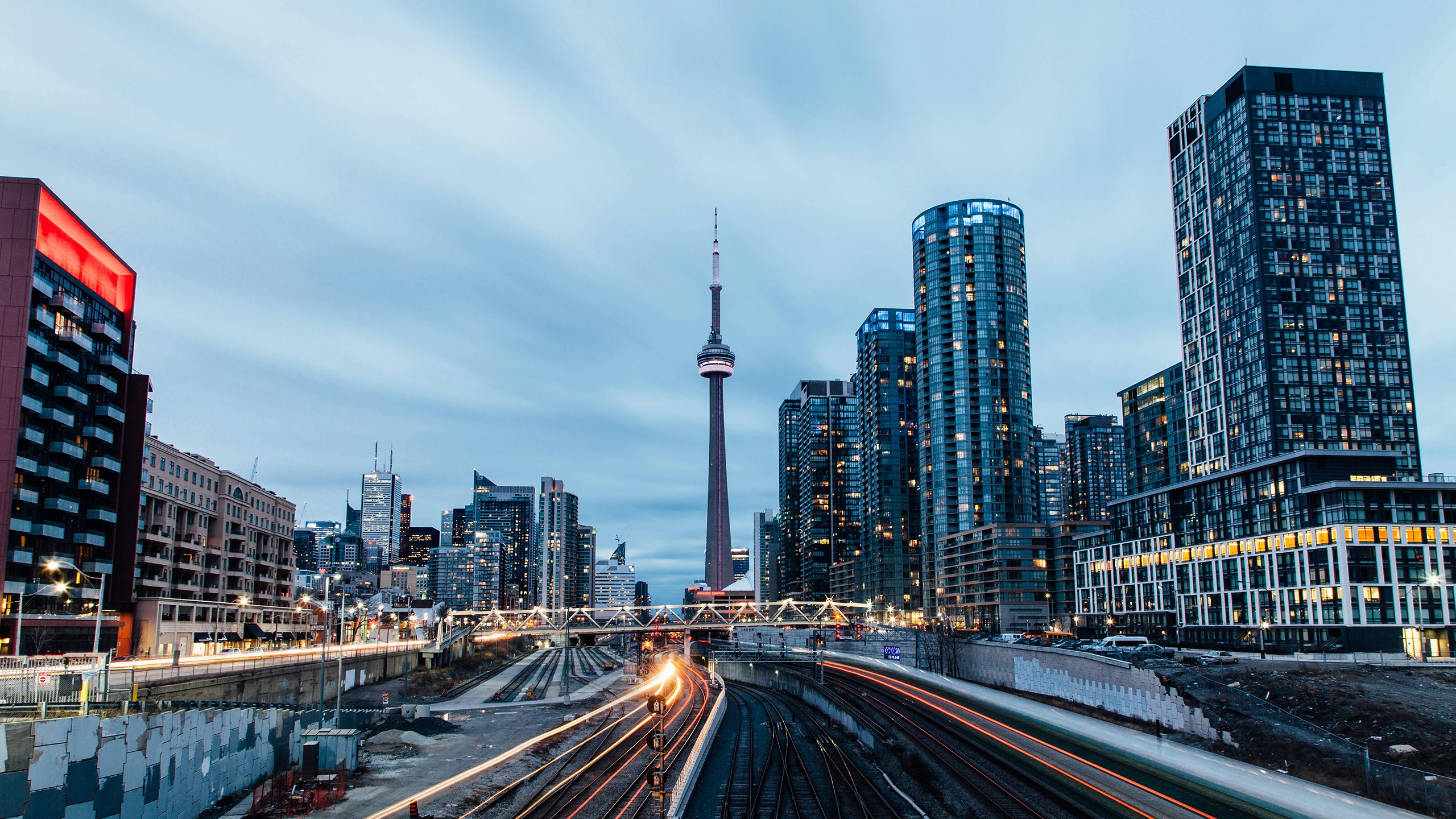 Toronto cityscape at dusk featuring modern high-rise buildings, with railway tracks leading towards the skyline.