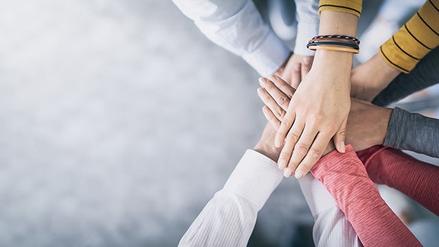 Diverse hands stacked together in a circle, representing teamwork, unity, and collaboration