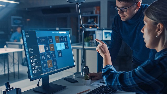 A person is standing in front of a screen displaying a graph with a blue line and a red line.