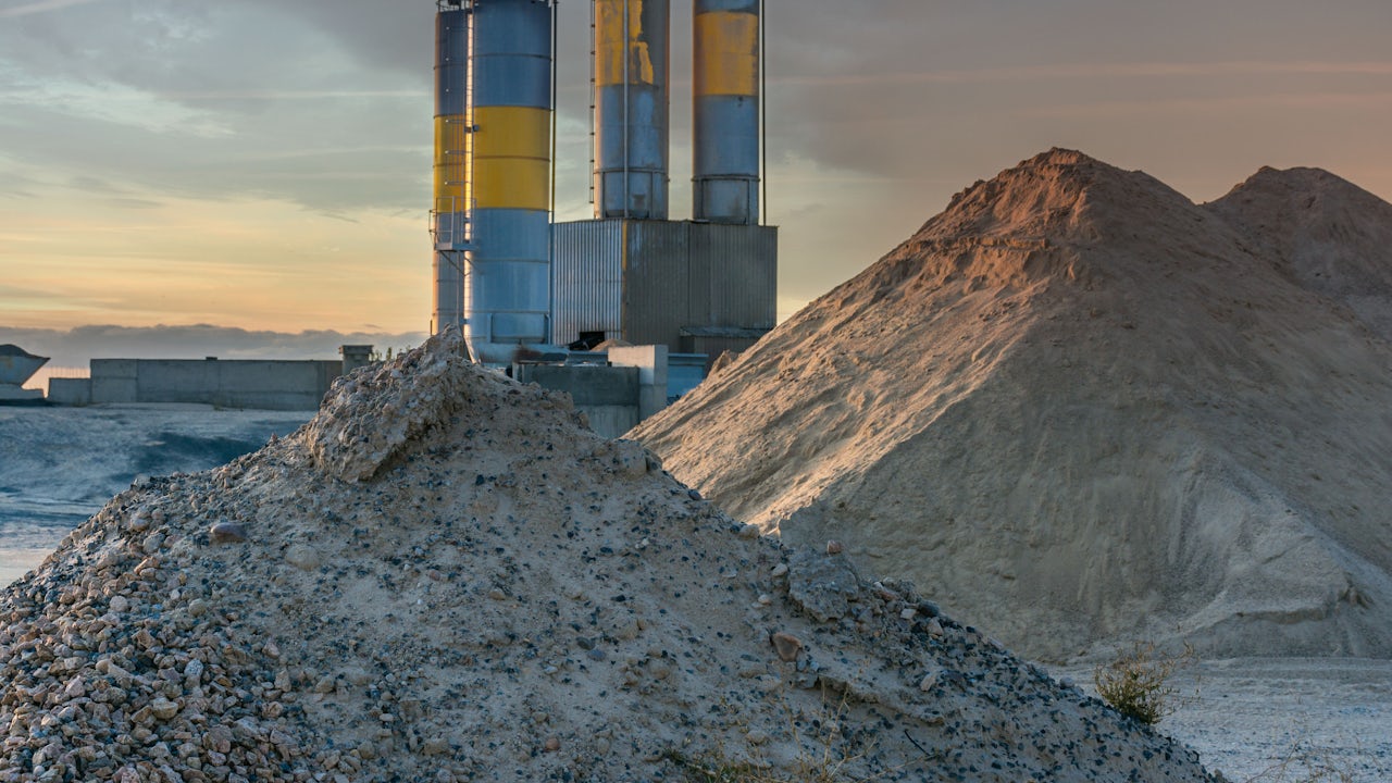 A cement manufacturing plant with a large building and machinery in the foreground.