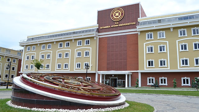 A modern university building with a large entrance and a clock tower in the background.
