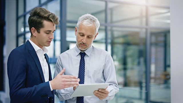 Two men having a conversation about information shown on a tablet device.