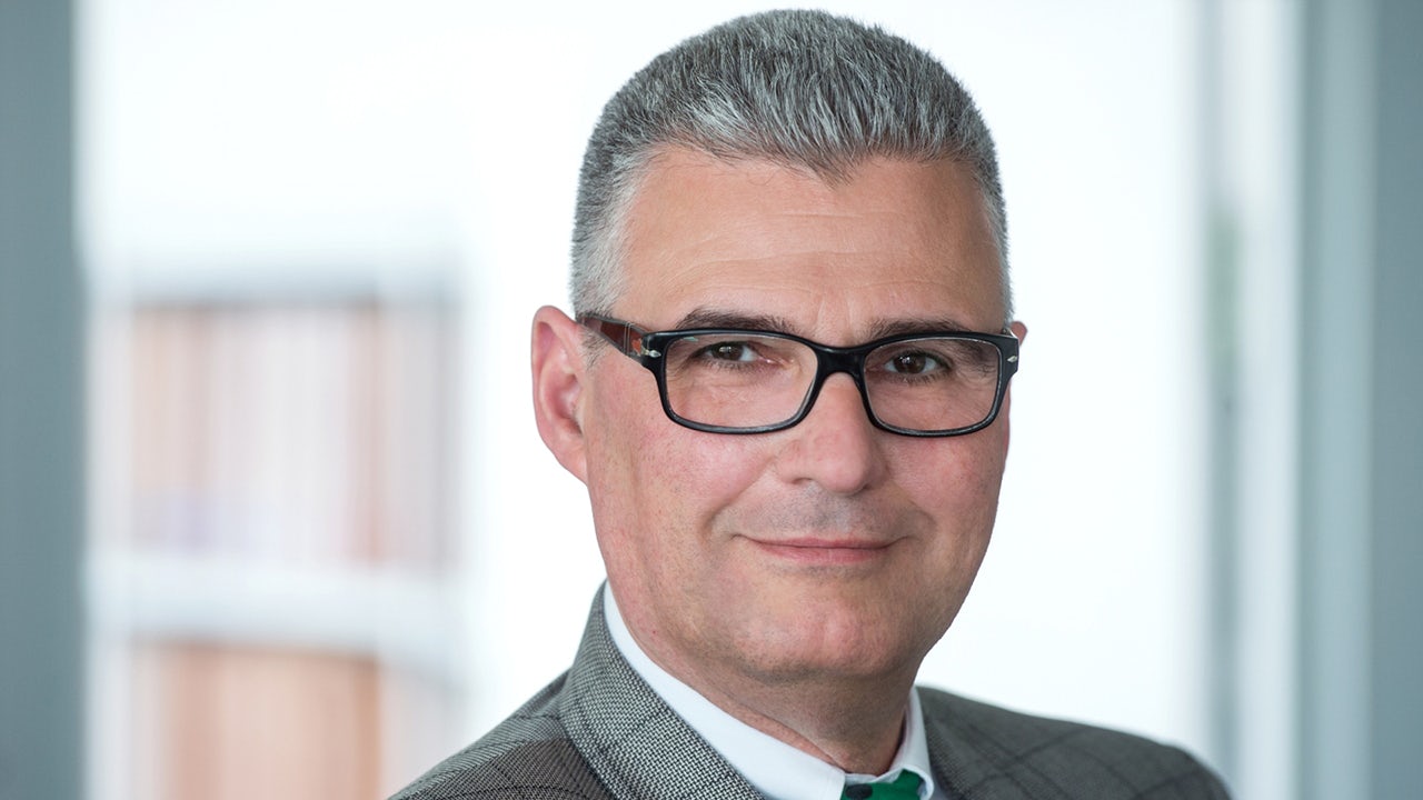 Josef Mehl, a representative of Siemens Fonds Invest Mhero, stands in front of a Siemens building, smiling at the camera.