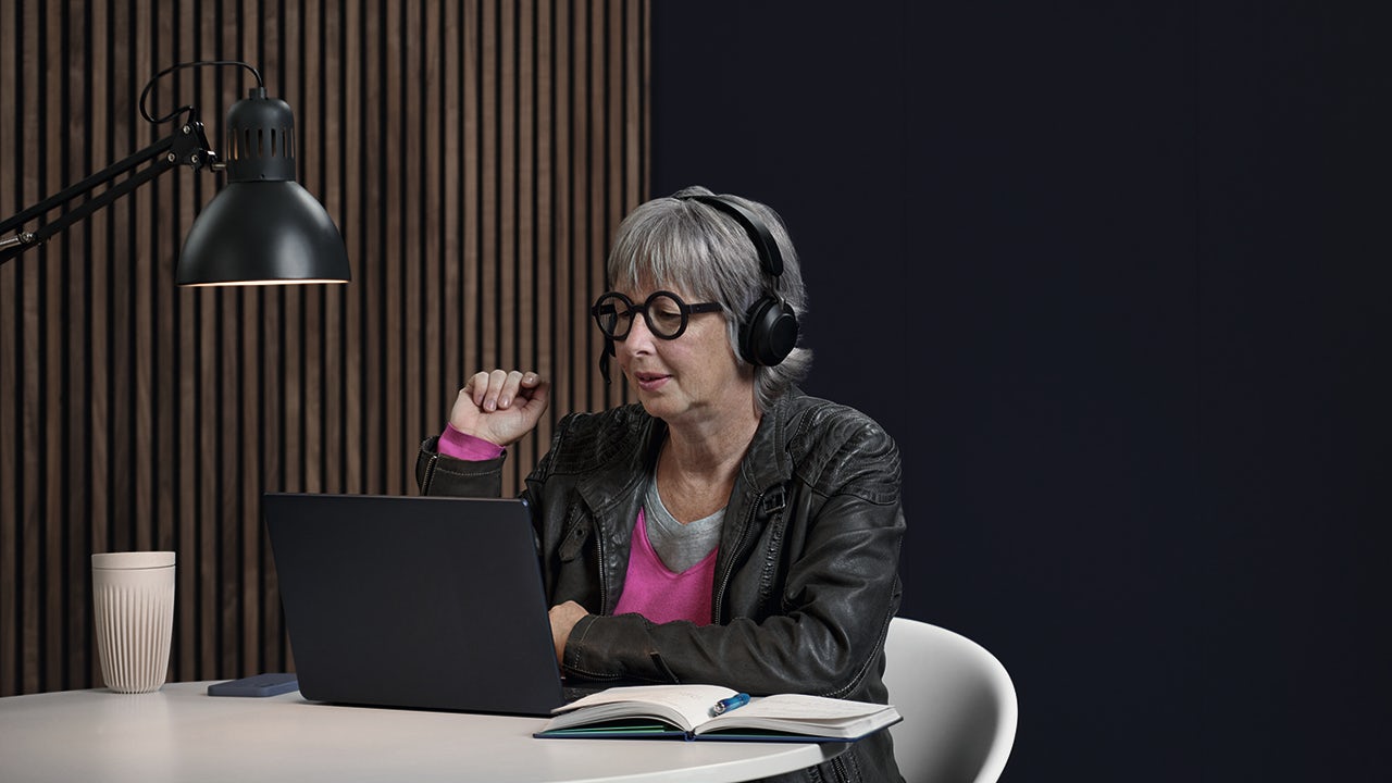 A person in their 50s is standing in front of a white wall, wearing a black shirt and a smile on their face.