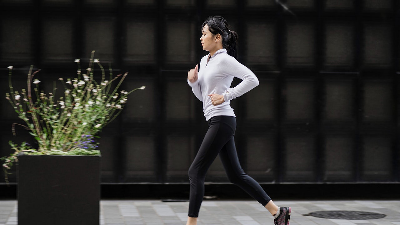 Person balancing on one leg on a wooden dock by a lake, arms outstretched, with mountains in the background
