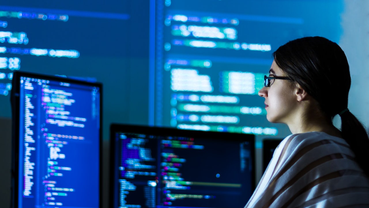 A software developer is working on a computer with a cybersecurity theme on the screen.