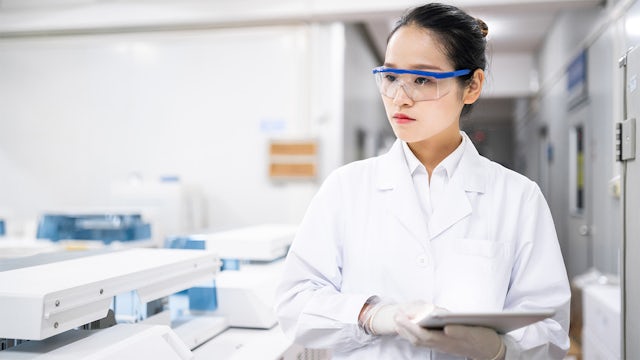 A woman in a medical device manufacturing facility wears safety glasses and gloves while holding a tablet.