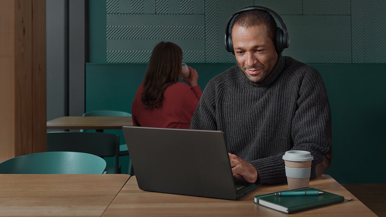 A person is standing in front of a desk with a laptop and a cup of coffee.