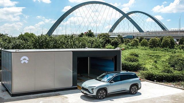 Blue electric car with sleek design parked on a road with trees in background