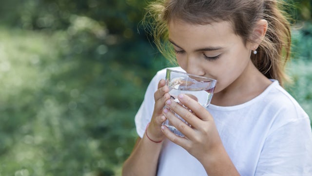 A young girl drinking a glass of water. 