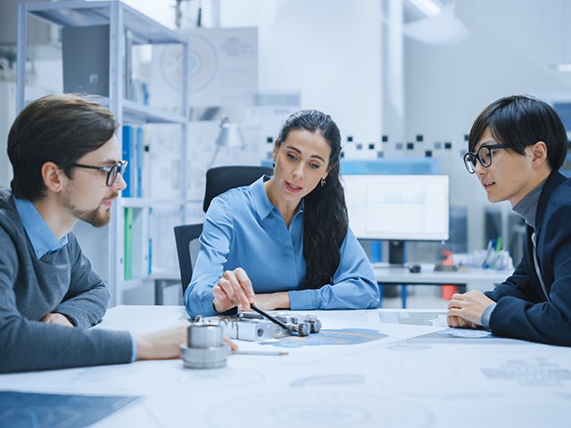Diverse team of industrial robotics engineers gathered around table with robot arm.