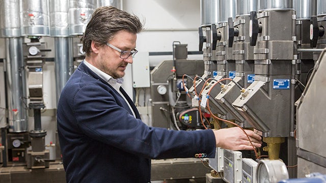 Man in blue shirt working on laptop at desk with window view